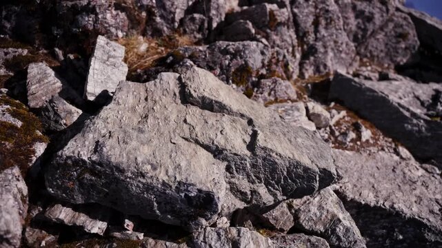 Close up handheld shaky view of flat layered stone steps along a mountain ridge with dry grass beside a steep drop toward hazy brown Himalayan cliffs