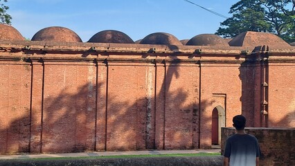 Historic red brick mosque structure with domes under clear blue sky © Your Design Master