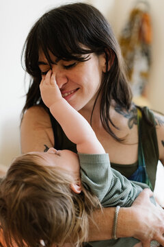 Toddler playfully covering their smiling mother's eye.