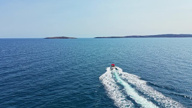 A boat travels through the blue water with white waves behind it. Small islands are seen in the distance under a clear sky. This scene shows a calm day on the water.