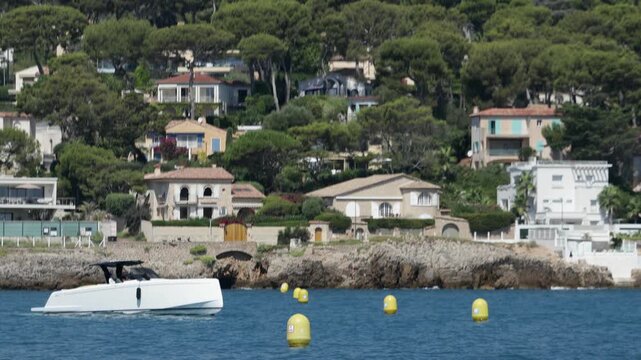 Small Yacht Cruising Along Mediterranean Coastline with Seaside Villas and Yellow Buoys near Antibes, French Riviera