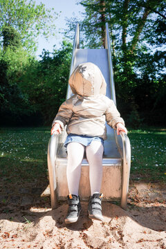 Hooded child sitting at bottom of metal slide