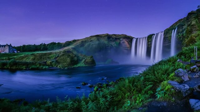 Time Lapse of Majestic Waterfall with Glowing Moonbow Rainbow Mist Under Starry Twilight Sky and Green Highland Landscape
