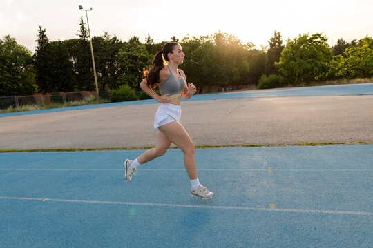 Young woman training on running track during sunset