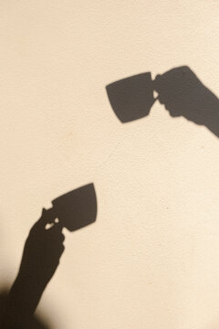 Shadows of hands holding coffee cups on sunny cafe wall