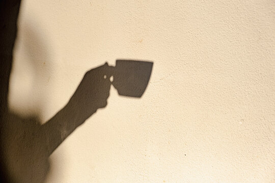Shadow of hand holding coffee cup on sunny cafe wall