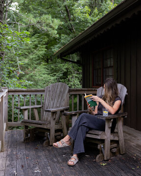 Woman Reading a Book in a Wooden Rocking Chair on a Porch