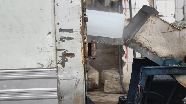 Large ice block sliding from a refrigerated truck into an ice crusher machine at a coastal fishing port