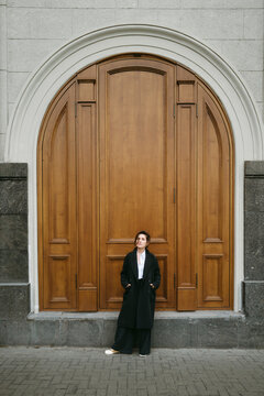 Standing Confidently by an Ornate Wooden Door in an Urban Setting