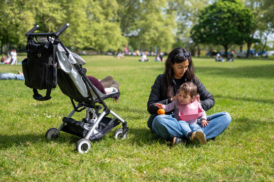 Mother Giving Baby Orange Snack On London Park Grass
