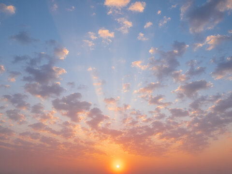 A beautiful sunrise illuminates the sky, casting golden rays through soft, scattered clouds during a peaceful morning dawn