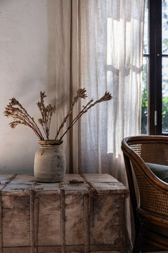 Warm interior vignette of vase, rattan chair and linen curtains