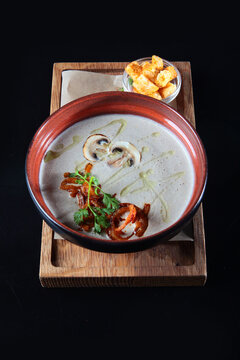 Creamy mushroom soup with croutons on wooden board. Creamy mushroom soup in ceramic bowl. Garnished with parsley, oil, pepper. Dark background. Wooden board. Healthy meal
