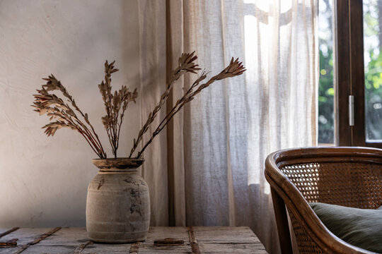Warm tones interior vignette of vase, rattan chair and linen curtain