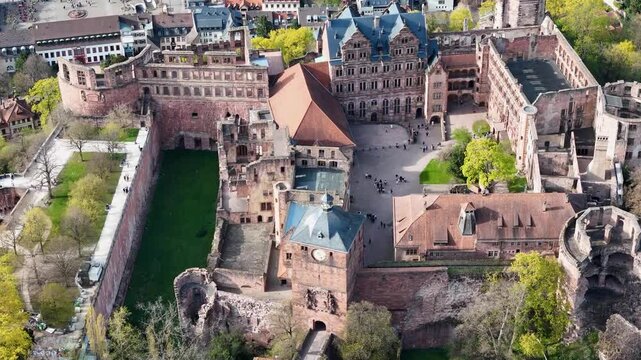 red sandstone castle ruins overlook heidelberg courtyard renaissance facade gothic tower moat garden terrace tourists walking plaza aerial pullback drone footage germany baden wurttemberg konigstuhl