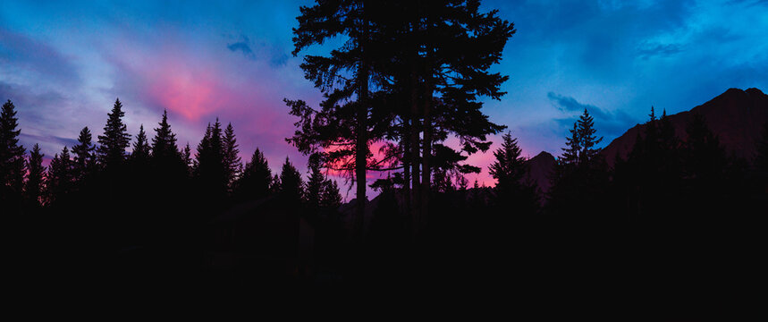 Mount Marathon sunrise panoramic landscape in Seward, Alaska, with pine tree forest, pink clouds in the blue sky, and mountain peaks in silhouette at Kenai Fjords National Park, USA