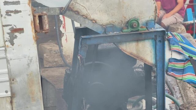 An industrial ice crusher processing a large ice block with a colorful striped canvas slide chute for ice delivery at a port