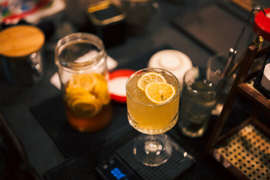 Orange cocktail in stemmed glass on bar counter with citrus garnish, mason jar, and cocktail tools creating warm atmosphere for beverage service and hospitality