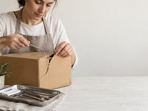 Person in an apron stitching a torn cardboard box with a surgical needle and thread, detailed repair with copy space for sustainability campaigns