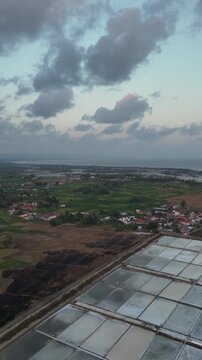 Aerial drone view of a diverse coastal landscape showing salt pans, green fields, a scorched earth patch, and a rural village by the sea at twilight