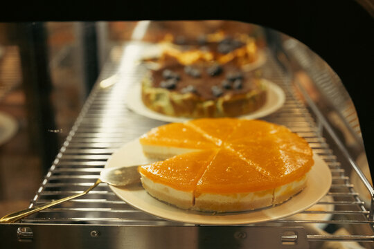 Orange cheesecake on cooling rack inside bakery oven with layered dessert in background