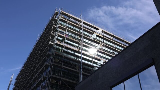 Modern building renovation with extensive scaffolding covering the facade as construction work upgrades exterior structure under bright blue sky in an urban district area