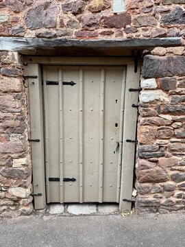 A rustic green wooden door in an ancient stone wall with an aged wooden lintel above. England, UK