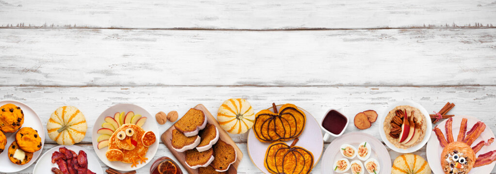 Fun Thanksgiving or fall breakfast or brunch foods. Top view bottom border on a white wood banner background. Pumpkin spice pancakes, loaf, muffins, turkey shaped pancakes and pastry. Copy space.