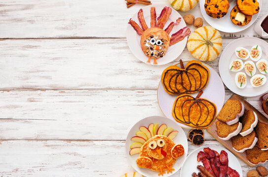 Fun Thanksgiving or fall breakfast or brunch foods. Top down view side border on a white wood background. Pumpkin spice pancakes, loaf, muffins, turkey shaped pancakes and pastry. Copy space.