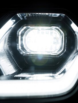 Modern car headlight shines brightly at night showing intricate detail. Futuristic auto lamp illuminates dark road ahead. Sleek design glows with led power.