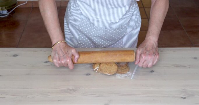 Crushing Dry Biscuits in a Freezer Bag with a Rolling Pin for Cheesecake Preparation. crushing dry biscuits inside a resealable plastic freezer bag using a rolling pin to for cheesecake.