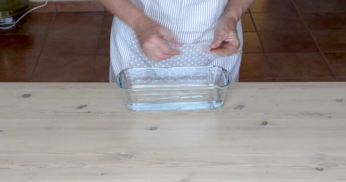 Soaking Gelatin Sheets in a Glass Bowl for Homemade Cheesecake Preparation. Close-up of female hands placing gelatin sheets into a small glass bowl filled with water to soften them for a cheesecake.