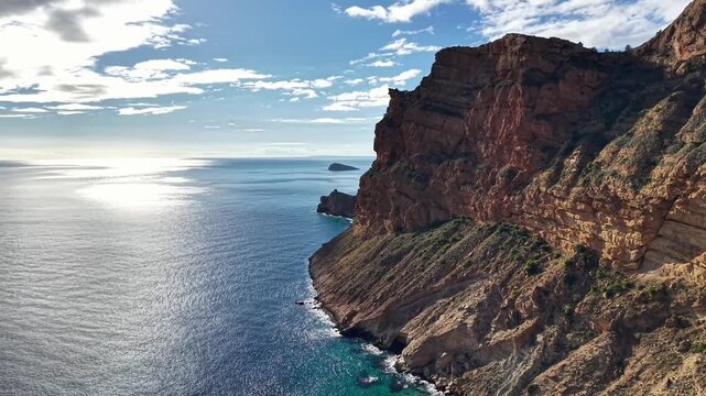 Aerial Cliff Coastline At Sunrise Shimmering Sea, Drone Pilot Filming Red Rock Face And Distant Islet, Calm
