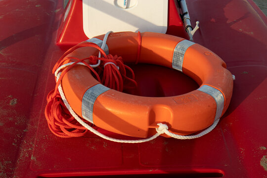 Salvagente anulare arancione con strisce catarifrangenti e sagola di recupero poggiato a bordo di un pattino di salvataggio rosso sulla spiaggia, attrezzatura professionale da bagnino per il soccorso 