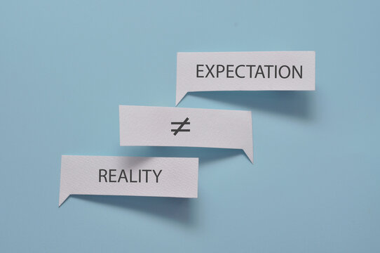 A composition made of paper with the words &ldquo;expectation&rdquo; and &ldquo;reality&rdquo; written on it, arranged around an inequality symbol, which symbolizes unfulfilled expectations.