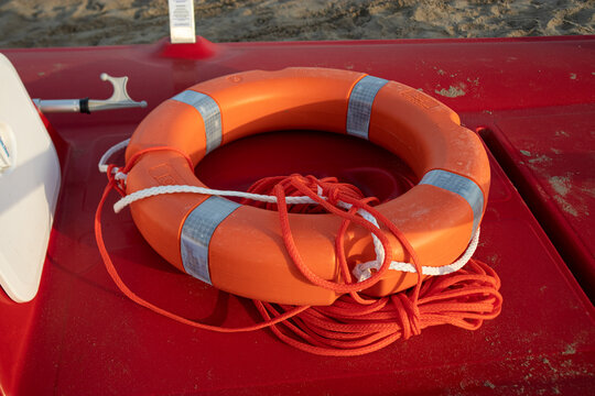 Salvagente anulare arancione con strisce catarifrangenti e sagola di recupero poggiato a bordo di un pattino di salvataggio rosso sulla spiaggia, attrezzatura professionale da bagnino per il soccorso 