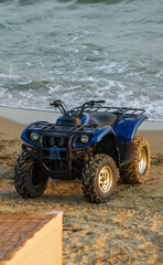 Blue ATV quad bike parked on the sandy sea beach by the ocean waves © Alexander
