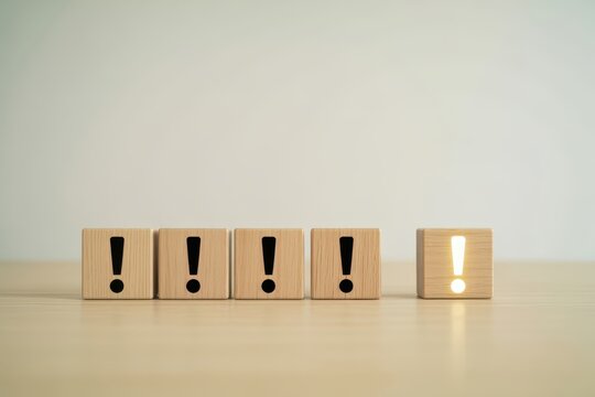 A glowing exclamation mark on wooden blocks among standard ones on a table. Great for problem solving and unique business ideas.