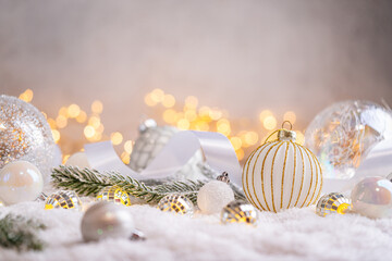 Naklejka premium A Christmas background featuring textured white and gold baubles alongside tiny mirror disco balls and frosted pine on snow, softly lit by warm twinkling lights with copy space.