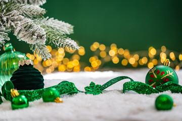 Naklejka premium A Christmas background featuring emerald baubles with gold filigree beneath a frosted pine branch, wrapped in glittering green ribbon on snow, set against deep green with twinkling lights.