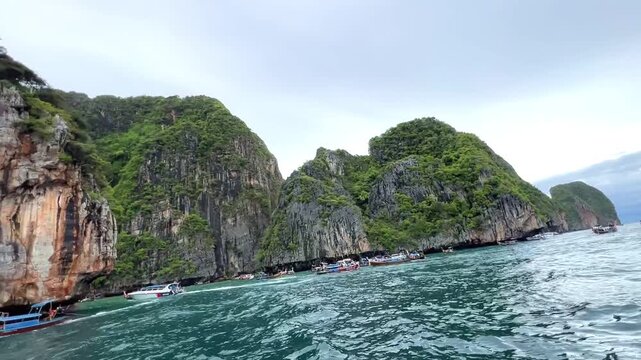 Phi Phi Island limestone cliffs above turquoise Andaman Sea near Phuket, Thailand, with tour boats along tropical coast, showcasing dramatic karst scenery, island travel and marine adventure landscape