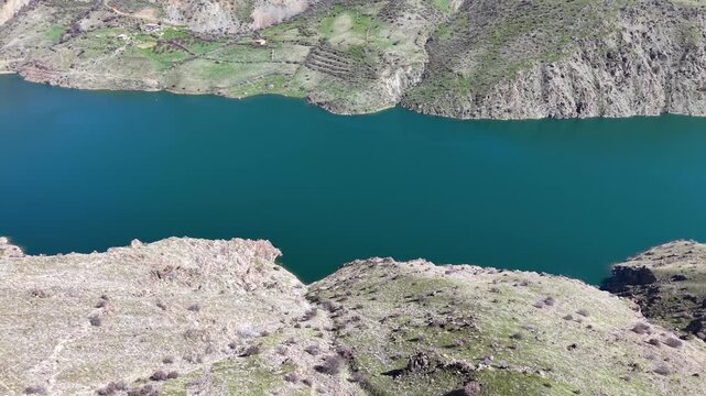 4K aerial drone shot flying close to a mountain slope, turning right and descending smoothly toward a scenic lake below. Natural lighting, color grading friendly flat profile.