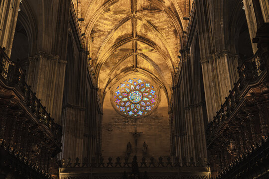 Stained glass rose window glowing above the crucifix in Seville Cathedral's Gothic nave