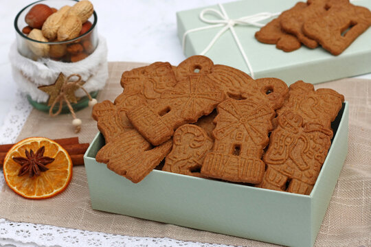Traditionelle Spekulatius-Kekse in einer hellgr&uuml;nen Geschenkbox mit winterlicher Dekoration, N&uuml;ssen und Zimtstangen.