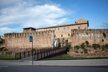 Obraz premium Veduta esterna di Castel Sismondo a Rimini con l'imponente bastione in mattoni e la passerella pedonale d'accesso moderna, architettura fortificata medievale sotto un cielo azzurro e nuvole