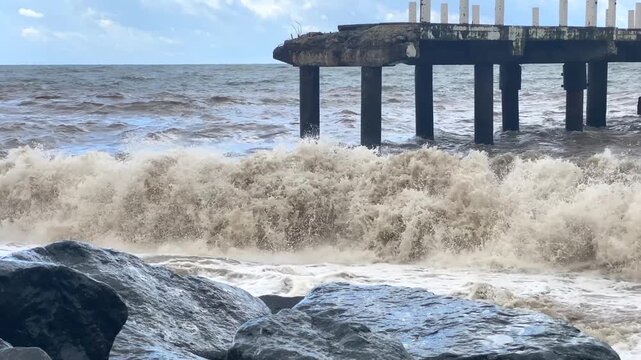 Sea waves hitting pier wide shot along a rocky coast, showing rough marine conditions for coastal risk, climate resilience, insurance, hazard planning and waterfront protection applications