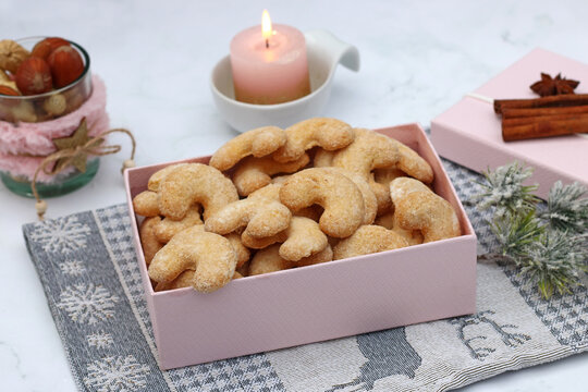  Fresh vanilla crescent cookies in a pink gift box with a lit pink candle and Christmas decorations.