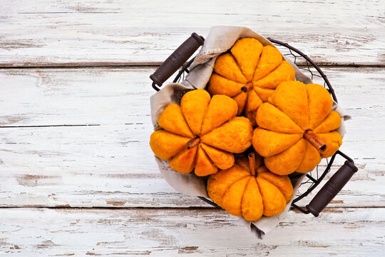 Basket of fall pumpkin shaped buns. Overhead view on a white wood background.