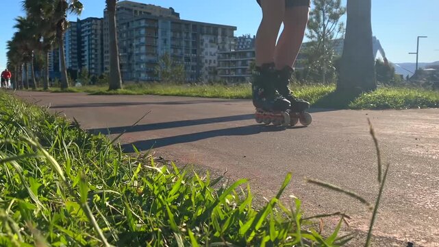 Woman rollerblading in low angle view along a paved park path in Batumi, with grass, palms and apartment buildings, suited for recreational fitness, urban leisure, active transport and tourism use 
