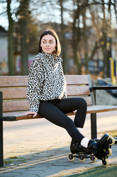 Woman relaxing in skates beside walkway, seated on wooden bench in peaceful outdoor setting